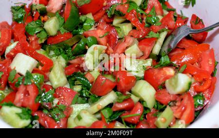 Grüner, gesunder, ökologischer/biologischer, frisch geschnittener Salat aus frischen Gemüseteilen und Scheiben von Tomaten, Gurken, Rucola-Blättern und Zwiebeln mit Kräutern und Olivenöl, Stockfoto