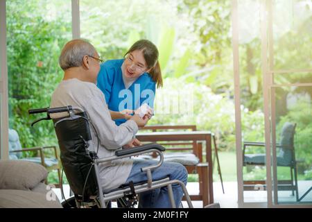 Asiatische junge Frau Krankenpflegepillen mit Hilfe verschreibt älteren behinderten Patienten im Rollstuhl, wenn ältere Mann Stockfoto