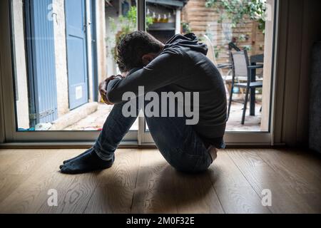 Deprimierter Mann. Trauriger unglücklicher Mann, der auf dem Boden sitzt und seinen Kopf zwischen den Beinen hält Stockfoto