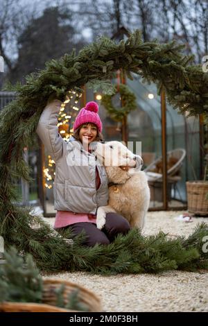 Eine Frau mit einem Hund im Weihnachtskranz im Garten Stockfoto
