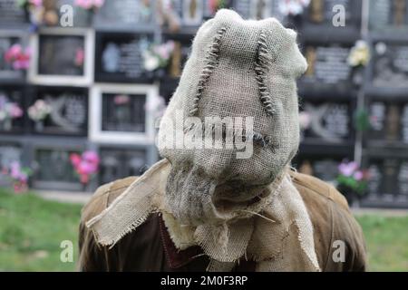 Gruseliger maskierter Mann am Friedhofseingang Stockfoto