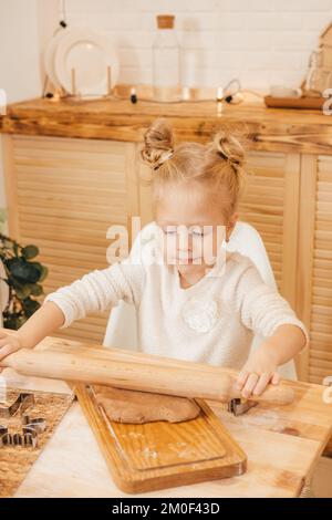 Mädchenhände Rollen Ingwerteig mit einem Nudelholz in der Küche aus. Mädchen bereitet weihnachtskekse auf einem Holztisch zu Stockfoto