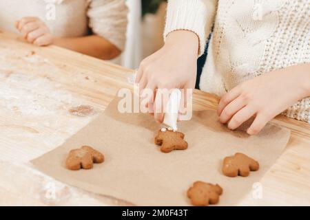 Nahaufnahme von weiblichen Händen mit Glasur, die Lebkekse schmücken. Vorbereitung auf Weihnachten, Neujahr. Stockfoto