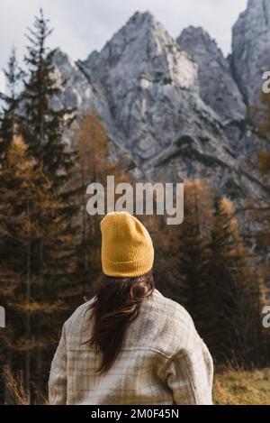 Rückansicht einer jungen Frau in Herbstkleidung, die im Herbst unter wunderschönen Bergen steht Stockfoto