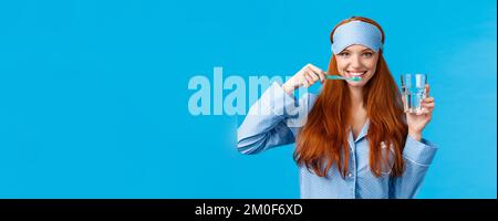 Enthusiastisch optimistisch, lebhaft Rothaarige Frau, Füchsin mit einem hübschen Lächeln, Zähneputzen mit Zahnbürste und Glaswasser, morgens aufwachen, immer Stockfoto