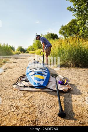 Man pumpt Stand-Up-Paddle-Boards SUP am Strand des Sees Sairan in der Stadt Almaty in Kasachstan. Stockfoto