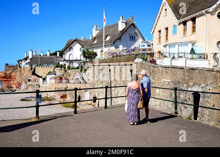 Blick auf traditionelle strohgedeckte Häuser mit Blick auf den Strand am Westende der Stadt, mit einem Paar im Vordergrund, Sidmouth, Devon, Großbritannien. Stockfoto