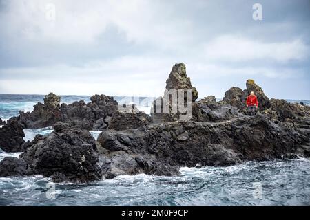 Ein Mann, der auf rauem vulkanischem Felsen an der Küste von São Jorge, Azoren, spaziert Stockfoto