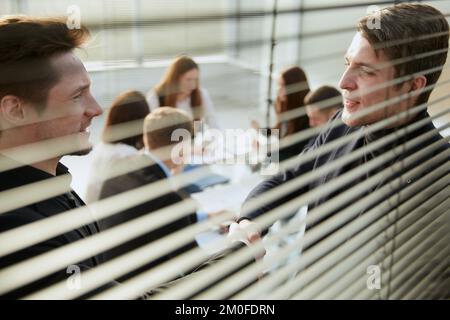 Durch die Jalousien. Kollegen aus der Wirtschaft schütteln sich die Hand . Stockfoto