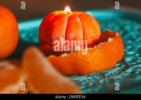 Eine brennende Kerze in Form einer Mandarine. Weihnachtsaufführung. Wunderschöne handgemachte Kerzen. Stockfoto