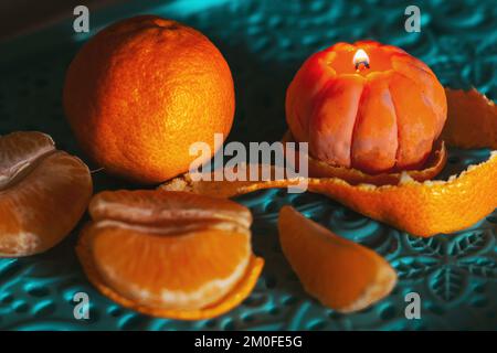 Eine brennende Kerze in Form einer Mandarine. Weihnachtsaufführung. Wunderschöne handgemachte Kerzen. Stockfoto