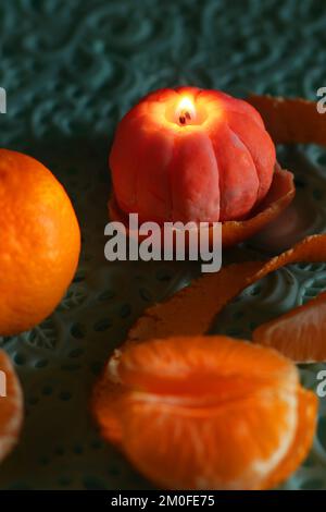 Eine brennende Kerze in Form einer Mandarine. Weihnachtsaufführung. Wunderschöne handgemachte Kerzen. Stockfoto