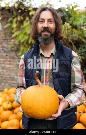 Bärtiger Bauer mit Kürbis auf einem Haufen Kürbisse Stockfoto