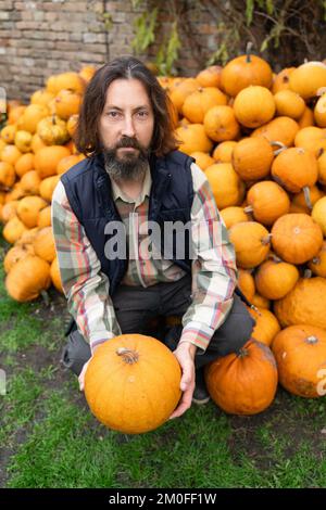 Bärtiger Bauer mit Kürbis auf einem Haufen Kürbisse Stockfoto