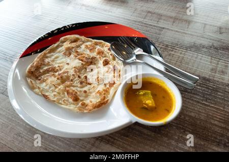 Nahaufnahme eines einfachen Roti Canai ohne Schnickschnack mit Dhal Curry auf einem Holztisch Stockfoto