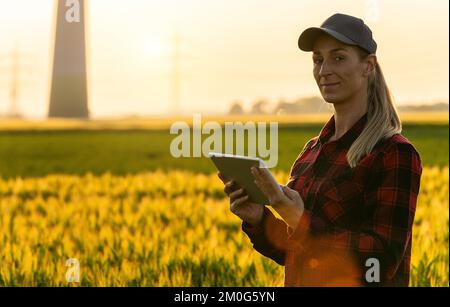 Glückliche Landwirtin untersucht das Getreidefeld und sendet Daten vom Tablet in die Cloud. Konzeptbild „Intelligente Landwirtschaft und digitale Landwirtschaft“ Stockfoto