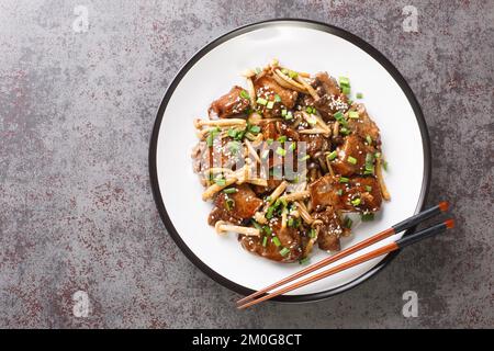 Asiatisches gebratenes Rindersteak mit Shimeji-Pilzen in Teriyaki-Sauce mit grünen Zwiebeln und Sesam aus nächster Nähe auf einem Teller auf dem Tisch. Horizontale Draufsicht von Stockfoto