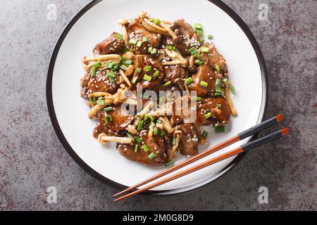 Japanische Küche, gebratenes Rindfleisch mit Buche-Pilzen in Teriyaki-Sauce mit grünen Zwiebeln und Sesam, Nahaufnahme auf einem Teller auf dem Tisch. Horizontal oben Stockfoto