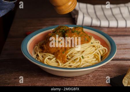 Nahaufnahme eines Tellers mit Fleischbällchen mit Spaghetti und Petersilie mit Pfeffer auf einem Holztisch Stockfoto