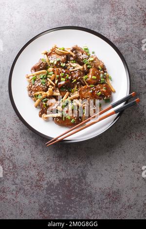 Rindersteak mit Buchenpilzen in Teriyaki-Sauce mit grünen Zwiebeln und Sesamsamen, Nahaufnahme auf einem Teller auf dem Tisch. Vertikale Draufsicht von Stockfoto