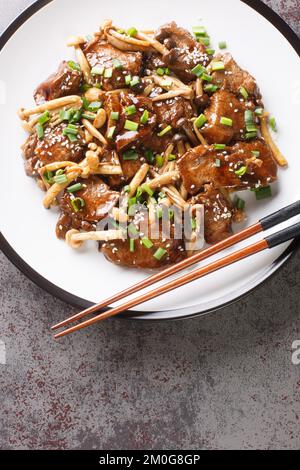 Japanisches Essen scharfes Teriyaki-Rindersteak in Sauce mit Pilzen auf dem Teller auf dem Tisch. Vertikale Draufsicht von oben Stockfoto