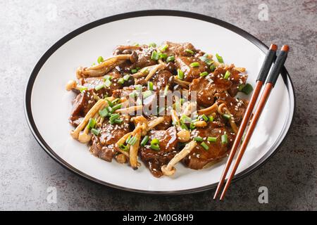 Asiatisches gebratenes Rindersteak mit Shimeji-Pilzen in Teriyaki-Sauce mit grünen Zwiebeln und Sesam aus nächster Nähe auf einem Teller auf dem Tisch. Horizontal Stockfoto