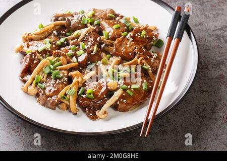 Japanische Küche, gebratenes Rindfleisch mit Buche-Pilzen in Teriyaki-Sauce mit grünen Zwiebeln und Sesam, Nahaufnahme auf einem Teller auf dem Tisch. Horizontal Stockfoto