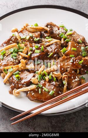 Rindersteak mit Buchenpilzen in Teriyaki-Sauce mit grünen Zwiebeln und Sesamsamen, Nahaufnahme auf einem Teller auf dem Tisch. Vertikal Stockfoto