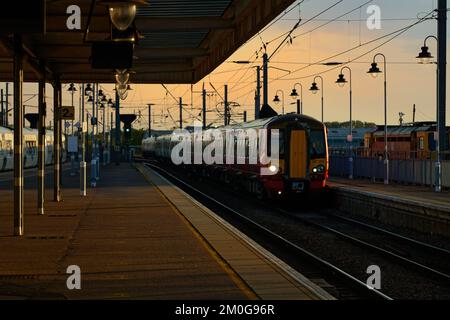 Ein elektrischer Zug der Greater Northern Klasse 387 in Rot ab der Gatwick Express-Lackierung wird bei Sonnenuntergang beim Betreten der Station Ely gesehen. Stockfoto