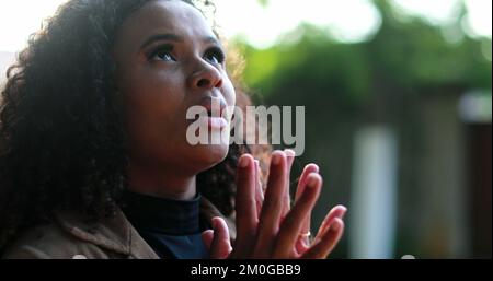 Eine afrikanische Frau betet draußen zu Gott und sucht im Sonnenlicht nach Hoffnung und Glauben Stockfoto