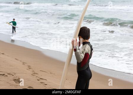 Castelldefels, Barcelona, Spanien - 9. Januar 2016: Zwei Freunde zwischen zehn und elf Jahren mit ihren Surfbrettern genießen einen bewölkten Wintertag, RE Stockfoto