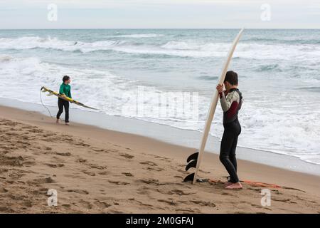 Castelldefels, Barcelona, Spanien - 9. Januar 2016: Zwei Freunde zwischen zehn und elf Jahren mit ihren Surfbrettern genießen einen bewölkten Wintertag, RE Stockfoto