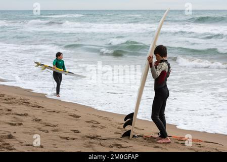 Castelldefels, Barcelona, Spanien - 9. Januar 2016: Zwei Freunde zwischen zehn und elf Jahren mit ihren Surfbrettern genießen einen bewölkten Wintertag, RE Stockfoto