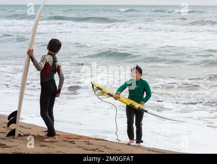 Castelldefels, Barcelona, Spanien - 9. Januar 2016: Zwei Freunde zwischen zehn und elf Jahren mit ihren Surfbrettern genießen einen bewölkten Wintertag, RE Stockfoto