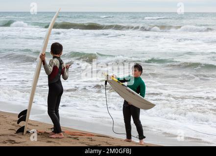 Castelldefels, Barcelona, Spanien - 9. Januar 2016: Zwei Freunde zwischen zehn und elf Jahren mit ihren Surfbrettern genießen einen bewölkten Wintertag, RE Stockfoto