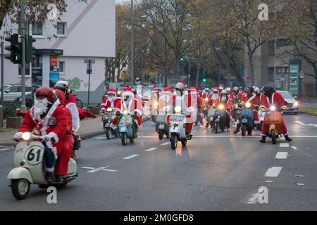 Mitglieder der Vespa-Motorroller-Clubs, die sich während einer Fahrt durch die Stadt Köln als Santas verkleidet haben. Die Roller sind beleuchtet und für Chri dekoriert Stockfoto