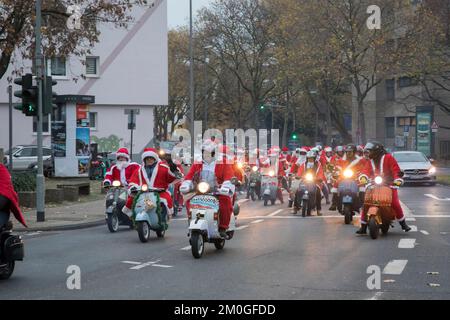 Mitglieder der Vespa-Motorroller-Clubs, die sich während einer Fahrt durch die Stadt Köln als Santas verkleidet haben. Die Roller sind beleuchtet und für Chri dekoriert Stockfoto