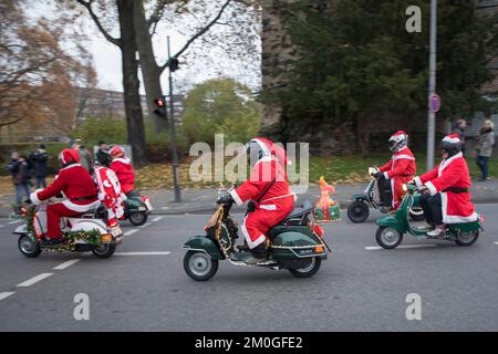 Mitglieder der Vespa-Motorroller-Clubs, die sich während einer Fahrt durch die Stadt Köln als Santas verkleidet haben. Die Roller sind beleuchtet und für Chri dekoriert Stockfoto