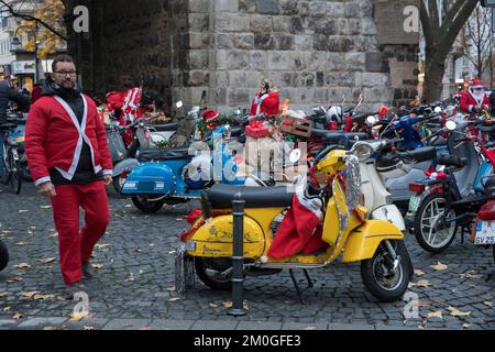 Mitglieder der Vespa-Motorroller-Clubs, die sich während einer Fahrt durch die Stadt Köln als Santas verkleidet haben. Die Roller sind beleuchtet und für Chri dekoriert Stockfoto