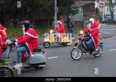 Mitglieder der Vespa-Motorroller-Clubs, die sich während einer Fahrt durch die Stadt Köln als Santas verkleidet haben. Die Roller sind beleuchtet und für Chri dekoriert Stockfoto