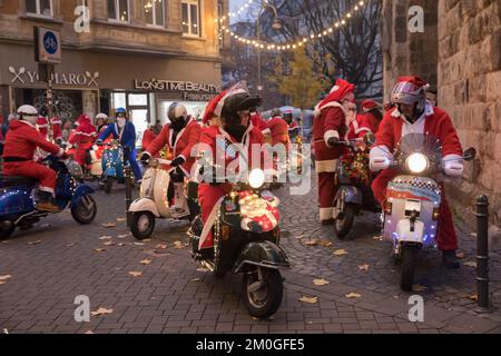 Mitglieder der Vespa-Motorroller-Clubs, die sich während einer Fahrt durch die Stadt Köln als Santas verkleidet haben. Die Roller sind beleuchtet und für Chri dekoriert Stockfoto