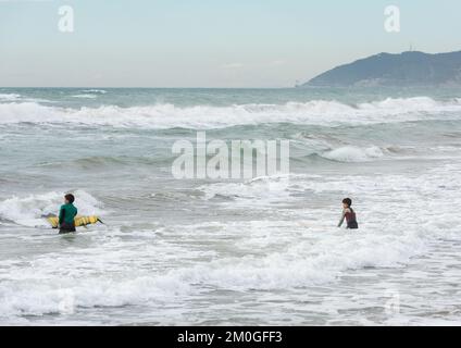 Castelldefels, Barcelona, Spanien - 9. Januar 2016: Zwei Freunde zwischen zehn und elf Jahren mit ihren Surfbrettern genießen einen bewölkten Wintertag Stockfoto