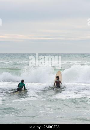 Castelldefels, Barcelona, Spanien - 9. Januar 2016: Zwei Freunde zwischen zehn und elf Jahren mit ihren Surfbrettern genießen einen bewölkten Wintertag Stockfoto