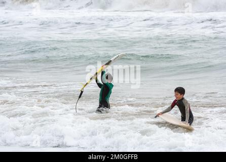 Castelldefels, Barcelona, Spanien - 9. Januar 2016: Zwei Freunde zwischen zehn und elf Jahren mit ihren Surfbrettern genießen einen bewölkten Wintertag Stockfoto