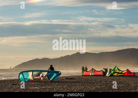 Castelldefels, Barcelona, Spanien - 9. Januar 2016: Eine Gruppe von Kitesurfern mit ihren Drachen wartet am Ufer eines breiten Strandes auf die Windbedingungen Stockfoto