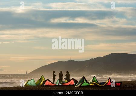 Castelldefels, Barcelona, Spanien - 9. Januar 2016: Eine Gruppe von Kitesurfern mit ihren Drachen wartet am Ufer eines breiten Strandes auf die Windbedingungen Stockfoto