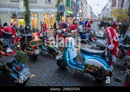 Mitglieder der Vespa-Motorroller-Clubs, die sich während einer Fahrt durch die Stadt Köln als Santas verkleidet haben. Die Roller sind beleuchtet und für Chri dekoriert Stockfoto