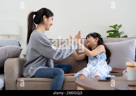 Porträt einer jungen Mutter und Tochter, die zu Hause geblasen werden. Glückliche mutter und Tochter, die sich mit Liebe auf dem Sofa umarmen Stockfoto