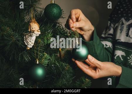 Einen weihnachtsbaum schmücken. Eine Nahaufnahme weiblicher Hände hängt einen grünen Ball an einen Ast Stockfoto