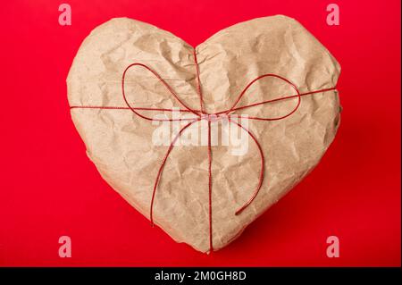 Herzförmige Geschenkbox in Kraftpapier auf rotem Hintergrund Stockfoto